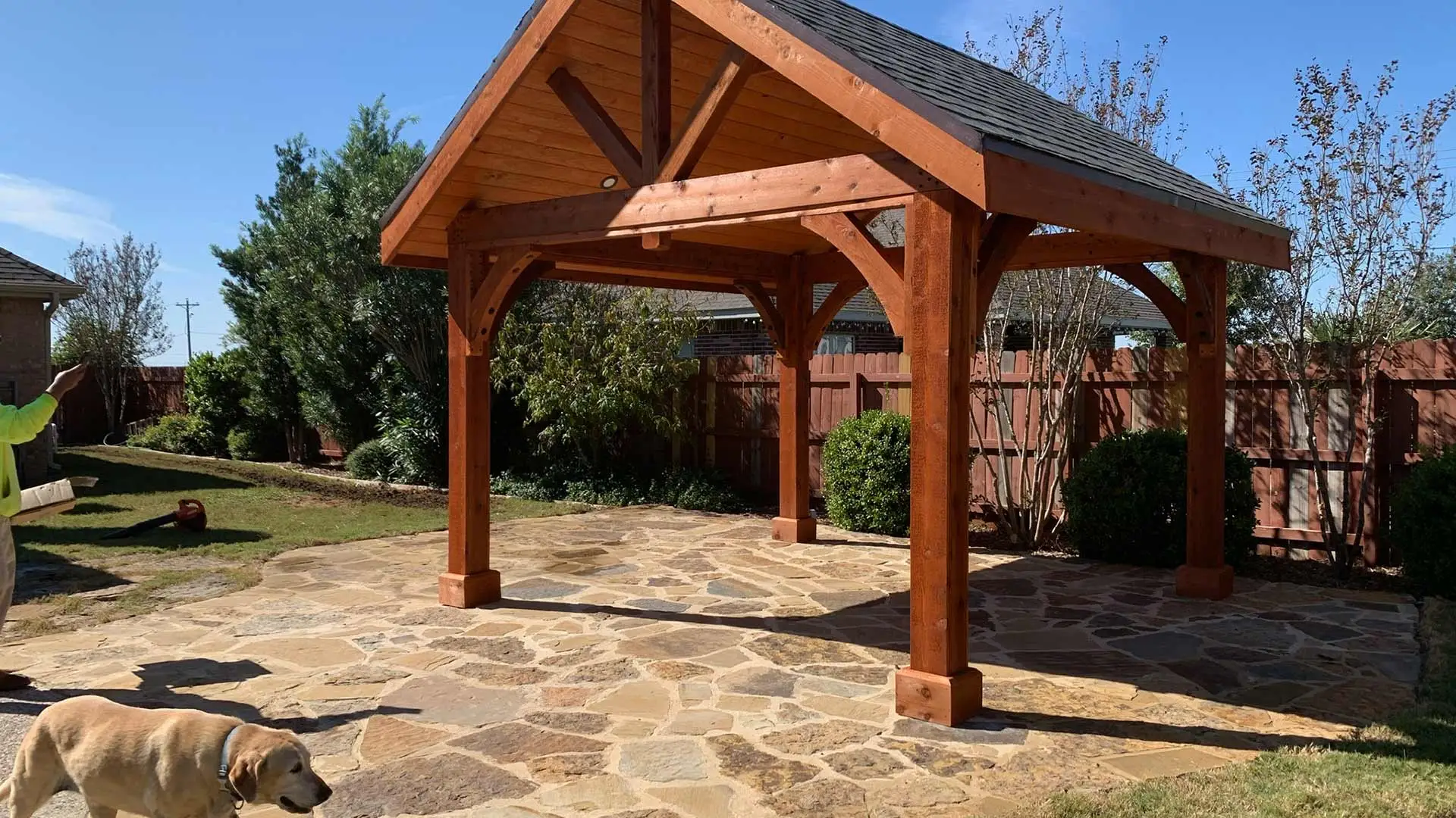 Red wood pergola and natural stone patio with a dog walking by near New Braunfels, TX.