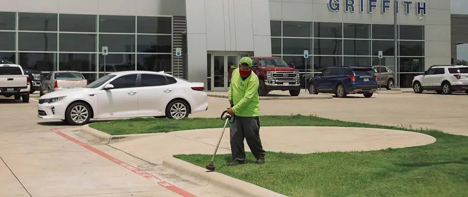 CLC Landscaping lawn care worker string trimming a commercial lot near New Braunfels, TX.