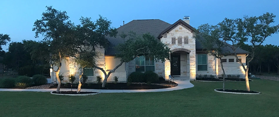 A white home in Buda, TX lit up in the evening thanks to our recently installed landscape lighting. 