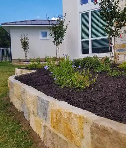 Dark mulch landscape bed with retaining wall in New Braunfels, TX.