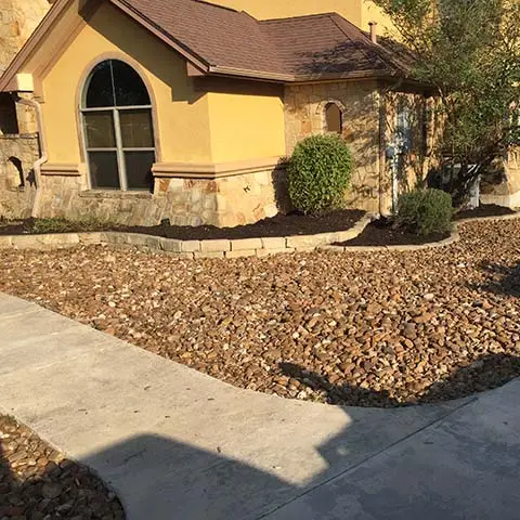 Red rock mulch and landscape beds around a home in Kyle, Texas.